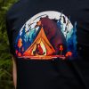 Close-up of a black T-shirt featuring a colorful design of a bear watching over a tent with a cub inside, surrounded by a forest under the moonlight.