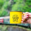 Yellow enamel camping mug with a camper van illustration and the word "Щастие" (Happiness), held by a hand with pink nail polish. Blurred train and green nature in the background.