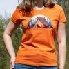 Woman wearing an orange fitted T-shirt with a camping-themed bear illustration, featuring a mother bear and cub near a tent and campfire.
