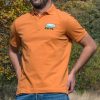 polo-teniska-s-yaka-oranzheva-myzhka Man wearing an orange polo T-shirt with an embroidered bear design featuring a mountain landscape.