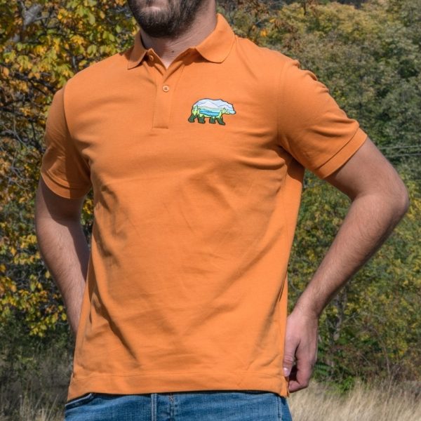 polo-teniska-s-yaka-oranzheva-myzhka Man wearing an orange polo T-shirt with an embroidered bear design featuring a mountain landscape.