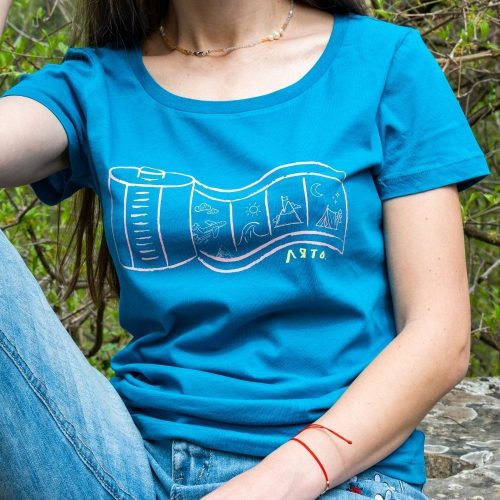 sinia-damska-teniska-za-planina-lyato Woman wearing a blue T-shirt with a summer-themed film roll design featuring waves, a lighthouse, mountains, and a camping scene.