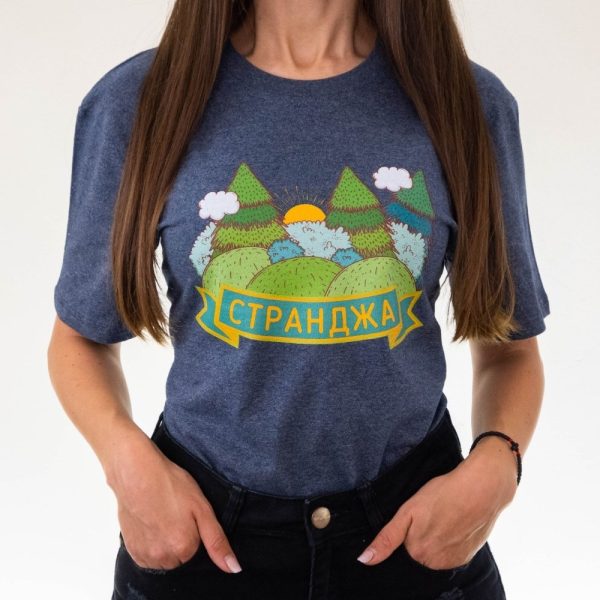 Woman wearing a dark gray unisex T-shirt featuring an illustration of Strandzha mountain, green hills, trees, clouds, and the text "Странджа" in Cyrillic.