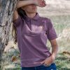 Woman wearing a muted mauve polo shirt with an embroidered bear design, leaning against a tree in a natural outdoor setting.