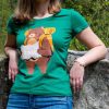 zelena-damska-teniska-mechka-s-ranitsa Woman wearing a green T-shirt featuring a design of a bear with a backpack holding a map, symbolizing adventure and exploration.