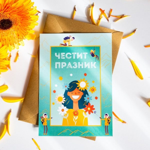 Podarak-za-momiche-zhena-planinarka (2) Colorful greeting card with the text "Честит празник" (Happy Holiday) featuring an illustration of a smiling woman with flowers in her hair, surrounded by mountain hikers, placed on a brown envelope with flower petals around.