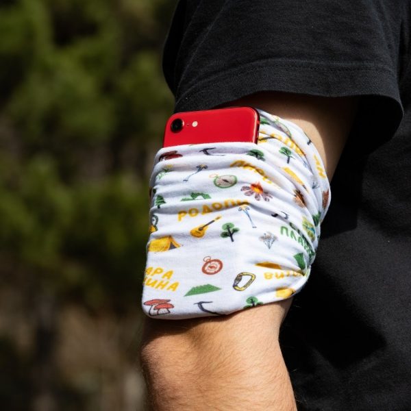 bandana-za-planina-buff A multifunctional white buff with Bulgarian mountain names and outdoor-themed illustrations, worn as an armband holding a red smartphone.