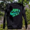 Black fleece sweatshirt with "HIKE – JUST DO IT" print, hanging on a tree branch in a natural setting.