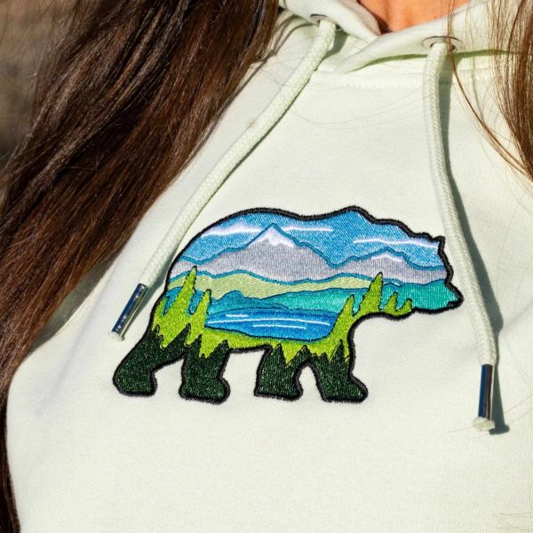 Close-up of a light green hoodie featuring an embroidered bear with a mountain landscape design.