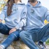 hoodie-s-kachulka-sinio Light blue hoodies with embroidered moose design, worn by a couple sitting outdoors.