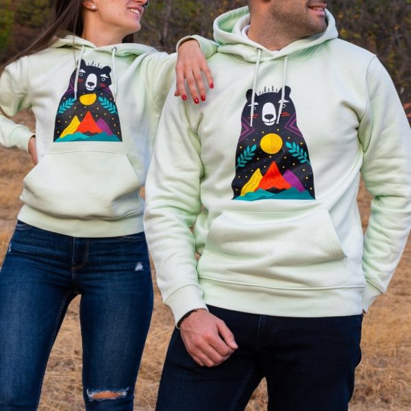 hoodie-sweatshirt-zelen-cvyat-menta Light green hoodie featuring a colorful bear and mountain design, worn by a smiling couple outdoors.
