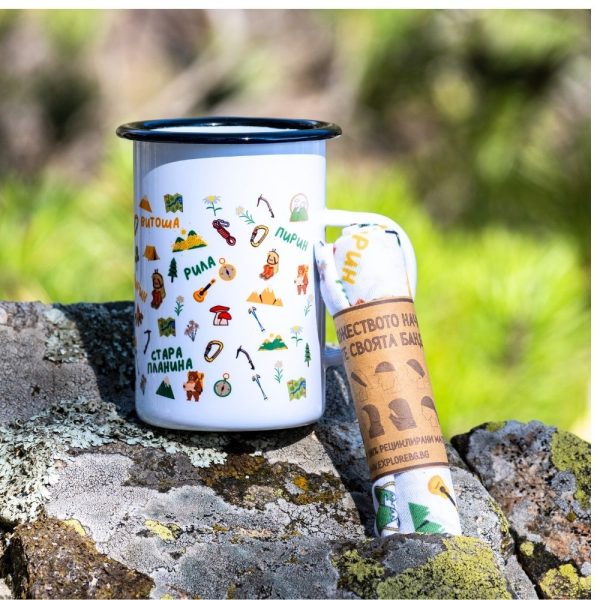 kanche-bandana-podarak-komplket-planinar (1) Large white enamel mug (450ml) with colorful illustrations of mountains, hiking gear, and a bear traveler, placed on a rock next to a rolled-up eco-friendly bandana.