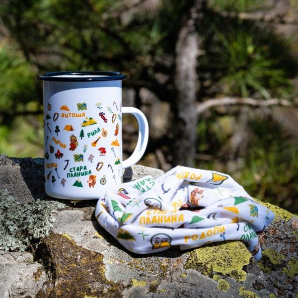 kanche-bandana-podarak-komplket-planinar (2) Large white enamel mug (450ml) with colorful illustrations of Bulgarian mountains and hiking symbols, placed on a rock next to a folded eco-friendly bandana.