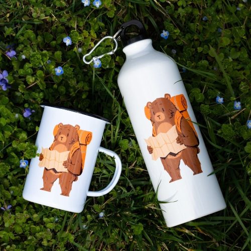 komplekt-mecho-turist-explorebg Large enamel mug (450ml) and aluminum bottle (800ml) featuring a hiking bear with a backpack and a map, lying on green grass with small blue flowers.