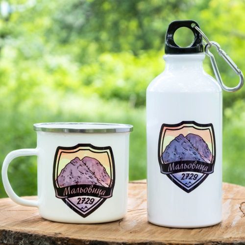 podarak-komplekt-butilka-kanche-malyovitsa White enamel mug and aluminum bottle with a design of Mount Malyovitsa (2729m), placed on a wooden surface with a green forest background.
