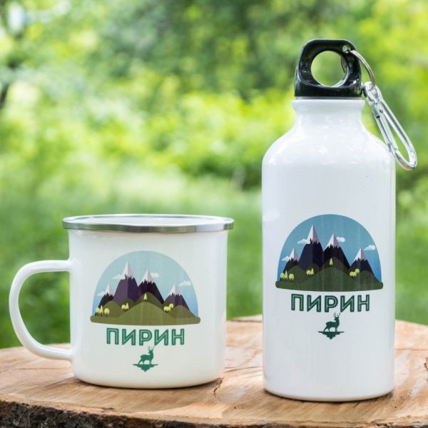 podarak-komplekt-butilka-kanche-pirin White enamel mug and 400ml aluminum bottle with a mountain-inspired design of Pirin, placed on a wooden surface with a green nature background.