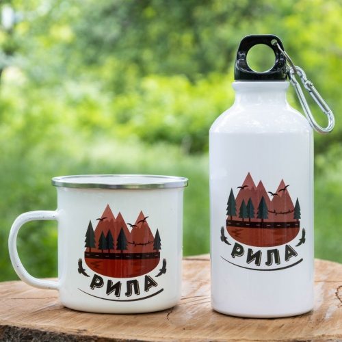 podarak-komplekt-butilka-kanche-rila White enamel mug and 400ml aluminum bottle with a scenic Rila Mountain design, placed on a wooden surface with a green nature background.