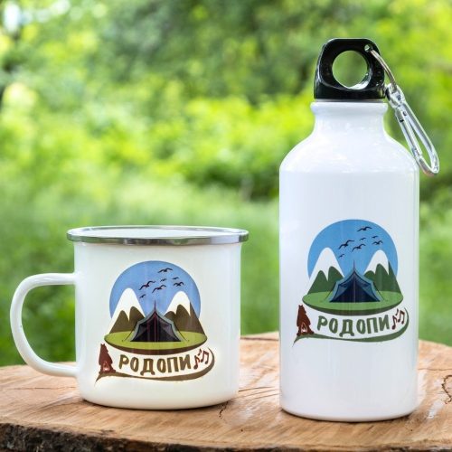 podarak-komplekt-butilka-kanche-rodopi White enamel mug and 400ml aluminum bottle with a scenic Rhodope Mountains design, placed on a wooden surface with a green nature background.