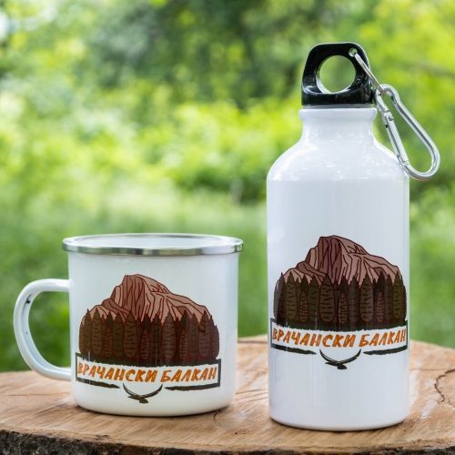 podarak-komplekt-butilka-kanche-vrachanski-balkan White enamel mug and 400ml aluminum bottle featuring a design of Vrachanski Balkan mountains, placed on a wooden surface with a green nature background.