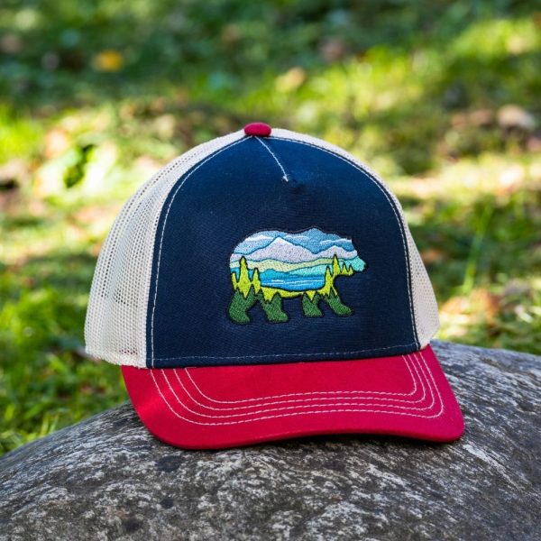 Trucker hat with an embroidered bear landscape design on the front, featuring a navy blue crown, red visor, and beige mesh back.