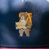 Close-up of an embroidered hiking bear holding a map on a navy and red cap.