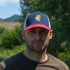 Man wearing a navy, red, and white trucker cap with an embroidered hiking bear holding a map.