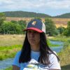 Woman wearing a navy, red, and white mesh cap with an embroidered hiking bear holding a map.