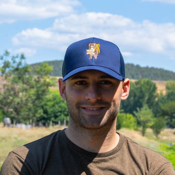 Man wearing a navy blue mesh cap with an embroidered hiking bear holding a map.