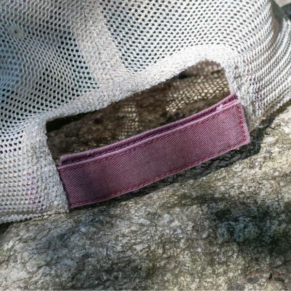 Close-up of the adjustable fabric strap and mesh back panel of a faded burgundy cap.