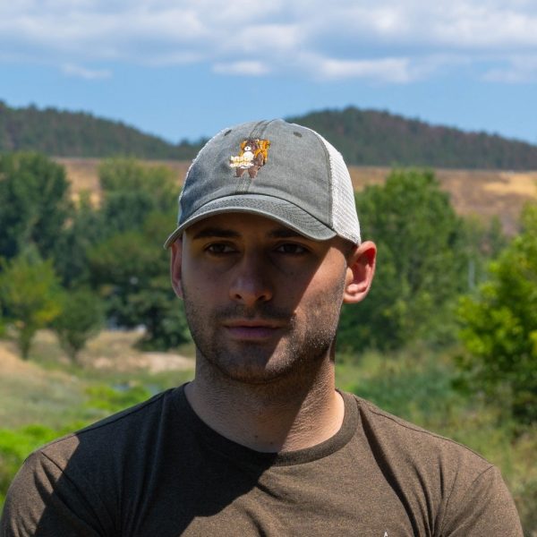 shapka-s-kozirka-meka-mrezha-zelena-myzhka Man wearing a vintage-style gray cap with an embroidered bear and a breathable mesh back.
