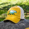 Yellow vintage trucker hat with embroidered bear holding a map, featuring a breathable mesh back and adjustable strap, placed on a rock outdoors.