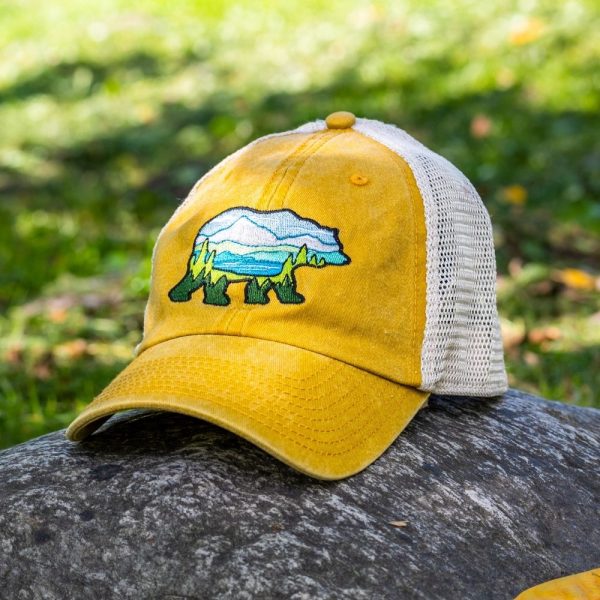 Yellow vintage trucker hat with embroidered bear holding a map, featuring a breathable mesh back and adjustable strap, placed on a rock outdoors.