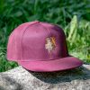 Burgundy snapback cap with an embroidered bear holding a map and wearing a backpack, placed on a rock in a natural setting.