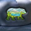 shapka-s-prava-kozirka-sinia Close-up of an embroidered bear landscape design on a navy blue trucker hat.