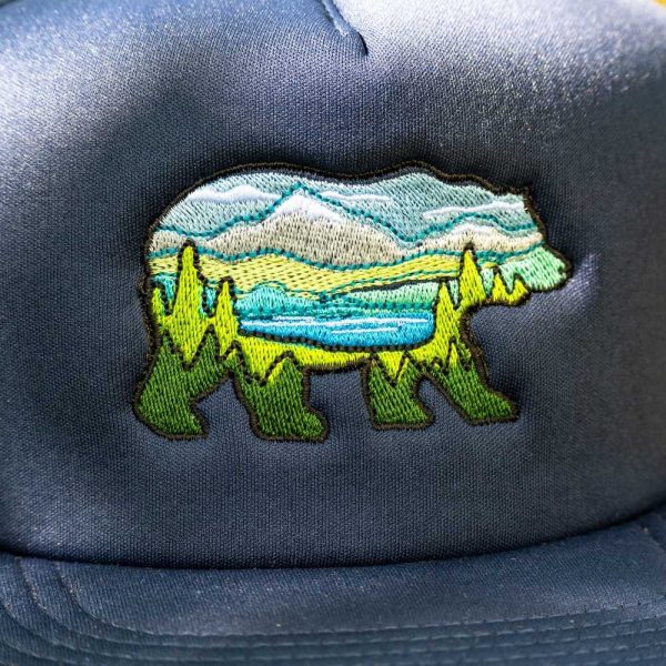 shapka-s-prava-kozirka-sinia Close-up of an embroidered bear landscape design on a navy blue trucker hat.