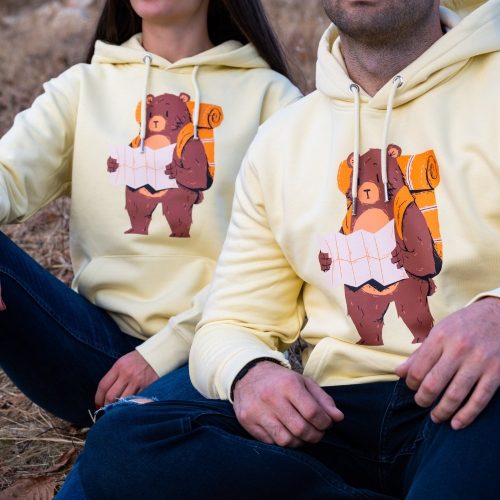 swearshirt-hoodie-zhylto Matching yellow hoodies with an illustrated hiking bear holding a map, worn by a couple sitting outdoors.