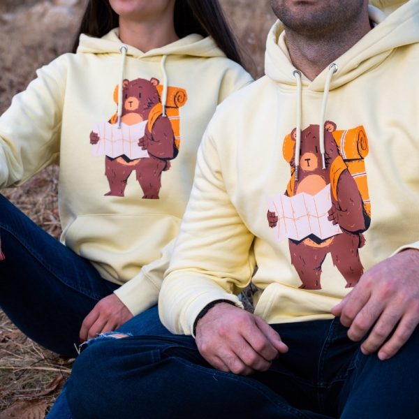swearshirt-hoodie-zhylto Matching yellow hoodies with an illustrated hiking bear holding a map, worn by a couple sitting outdoors.