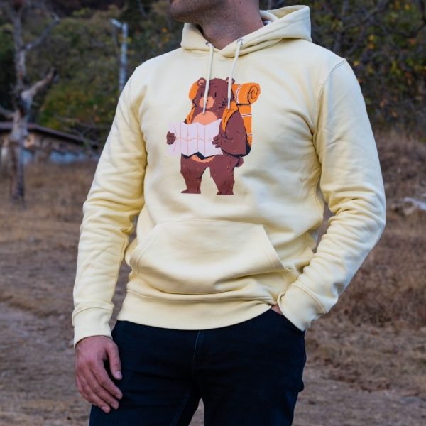 swearshirt-hoodie-zhylto-explorebg Yellow hoodie featuring a hiking bear print, worn by a man outdoors in a natural setting.
