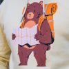 swearshirt-hoodie-zhylto-mechka Close-up of a yellow hoodie featuring a printed design of a hiking bear holding a map.