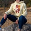 swearshirt-hoodie-zhylto-momiche Yellow hoodie with a hiking bear design, worn by a woman sitting on a rock outdoors.