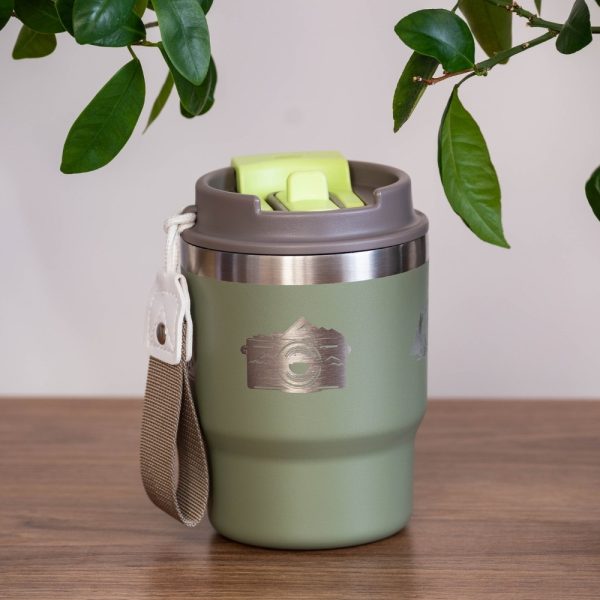 thermo-chasha-za-kafe-chai-engraving Green stainless steel thermal mug (350 ml) with a laser-engraved camera and nature design. Features a grey-green lid with a sliding lock mechanism and a fabric carrying strap.