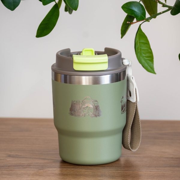 thermo-chasha-za-kafe-chai-fotoaparat Green stainless steel thermal mug (350 ml) with a laser-engraved camera and nature design. The lid is closed, featuring a green locking mechanism, and a carrying strap is attached to the side.