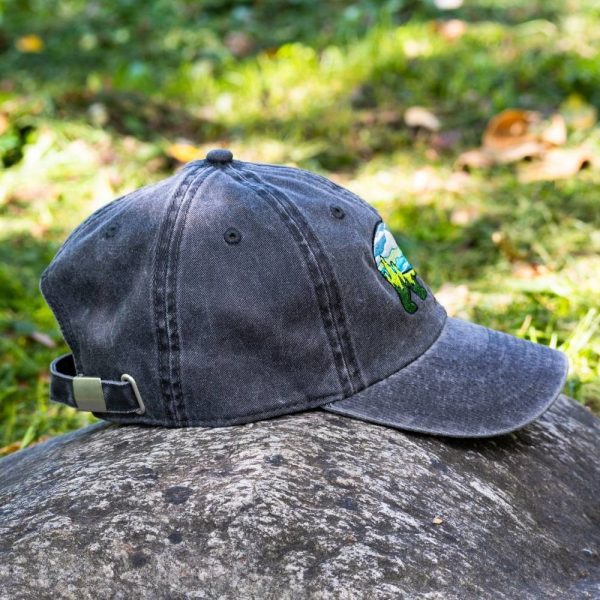 Vintage black baseball cap with an embroidered bear featuring a mountain landscape, placed on a rock in an outdoor setting.