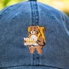 Close-up of a vintage blue baseball cap featuring an embroidered bear with a backpack and a map