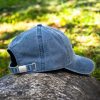 Back view of a vintage blue baseball cap with an adjustable metal strap, placed on a rock outdoors.