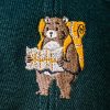 Close-up of embroidered bear with a backpack and map on a dark green baseball cap.