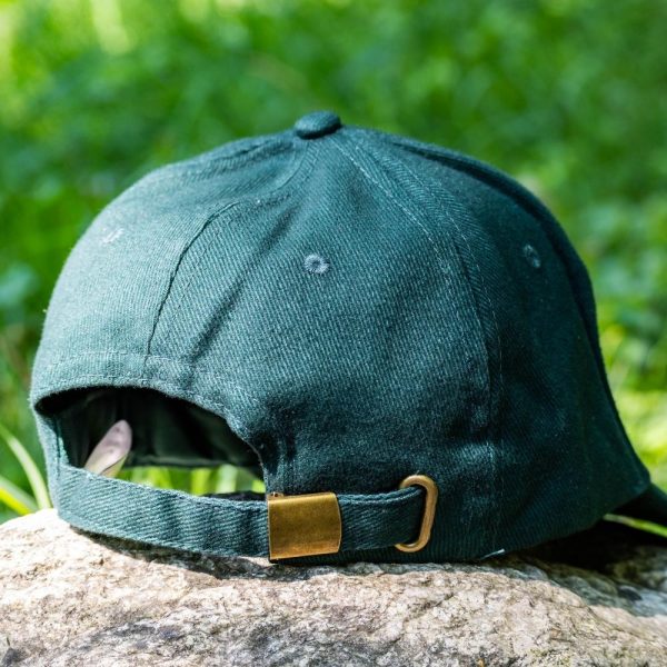 Back view of a dark green baseball cap with an adjustable brass buckle strap, placed on a rock with a blurred green nature background.