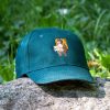 Vintage green baseball cap with an embroidered bear holding a map, placed on a rock outdoors.