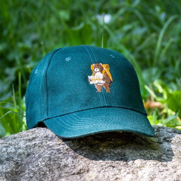 Vintage green baseball cap with an embroidered bear holding a map, placed on a rock outdoors.