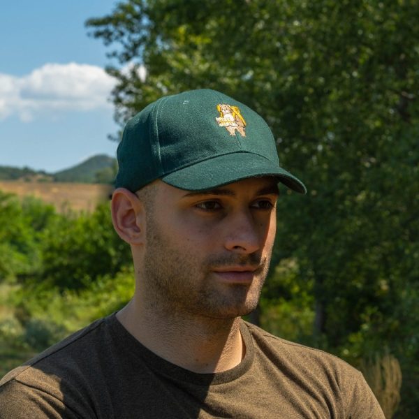 Man wearing a green baseball cap with an embroidered bear holding a map, outdoors with trees in the background.